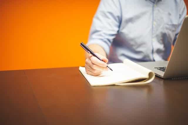 Man Writing on a Notebook and Using Laptop