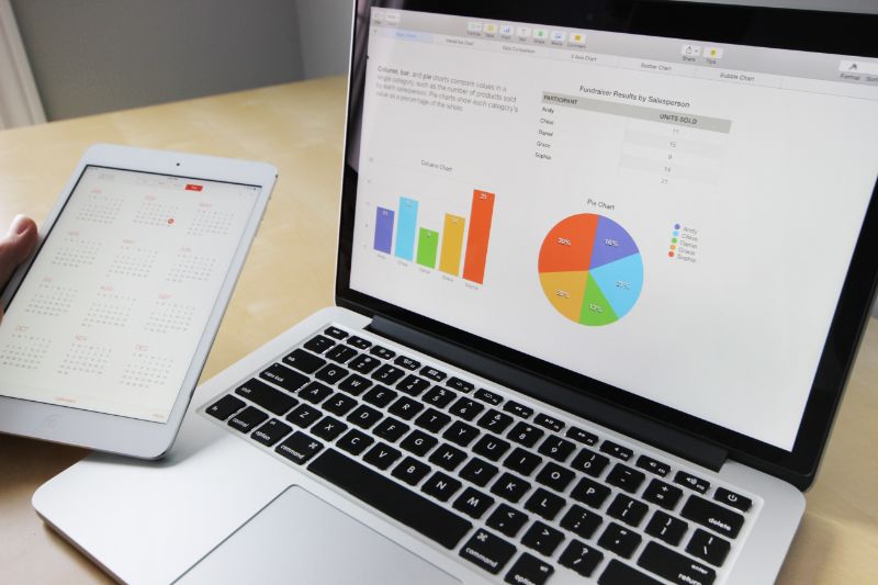 a person holding a tablet and reviewing reports on a laptop