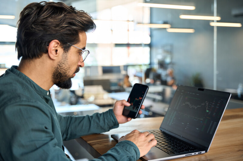 Stock trader looking at the trading  chart on a phone and laptop screen