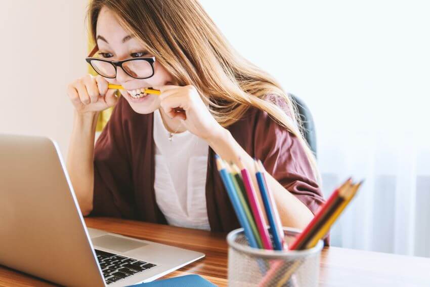 Girl working on laptop with a pencil in her mouth