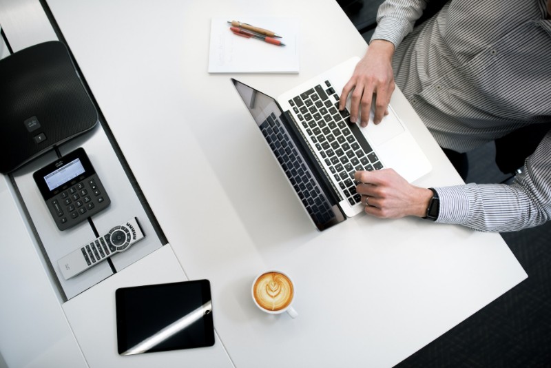 Freelance journalist typing on laptop on table with cup of coffee and notebook