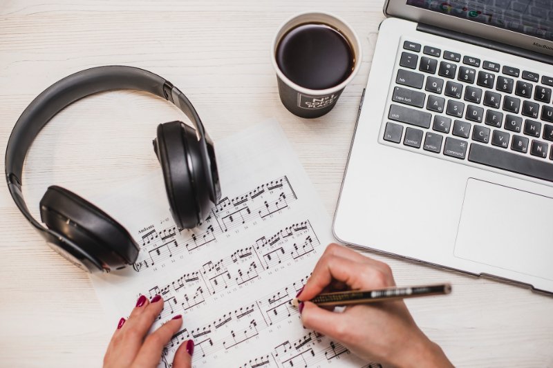 someone going through music notes with laptop and coffee on the table