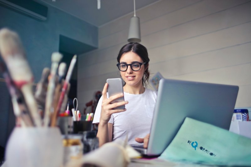 a lady looking at her phone while working on the laptop