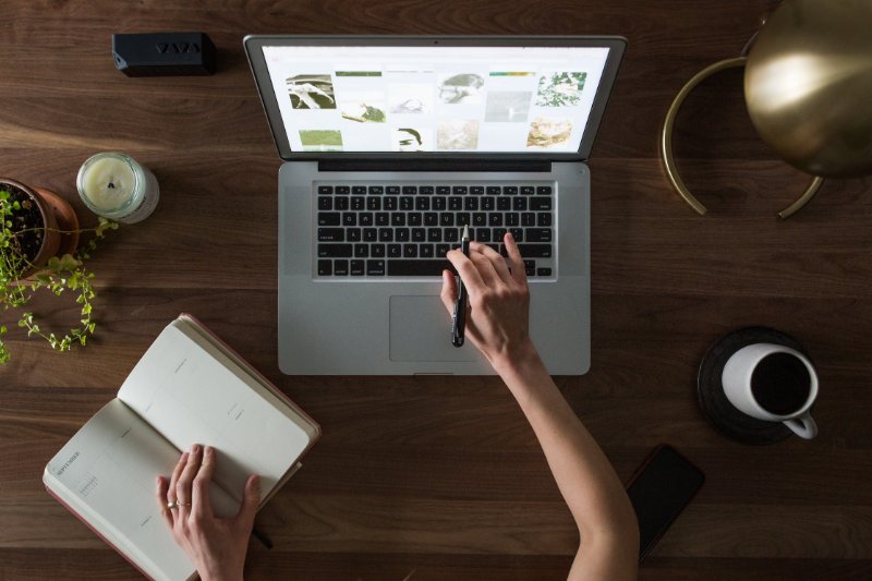 A person working on the laptop with a notebook and coffee on the table