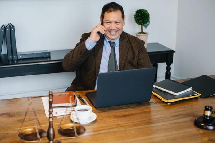 a man talking on the phone with his laptop, notebooks, and coffee mug placed on the table