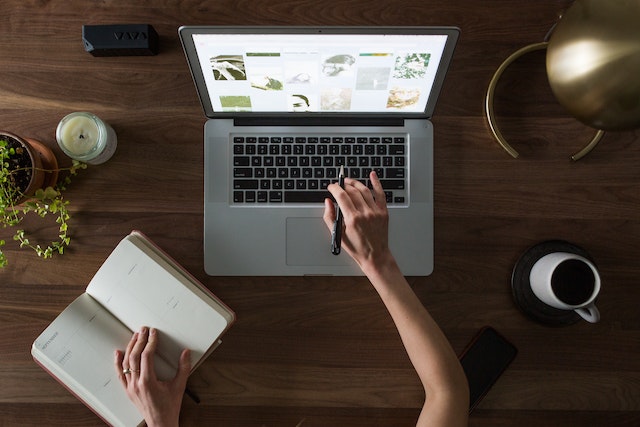 Person working on the laptop and using a notebook