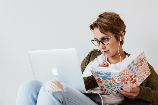 A girl watching something her on laptop with a notebook and pen in hands