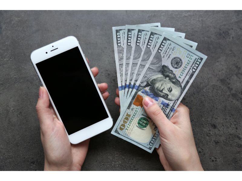 Hands holding smart phone with dollar banknotes