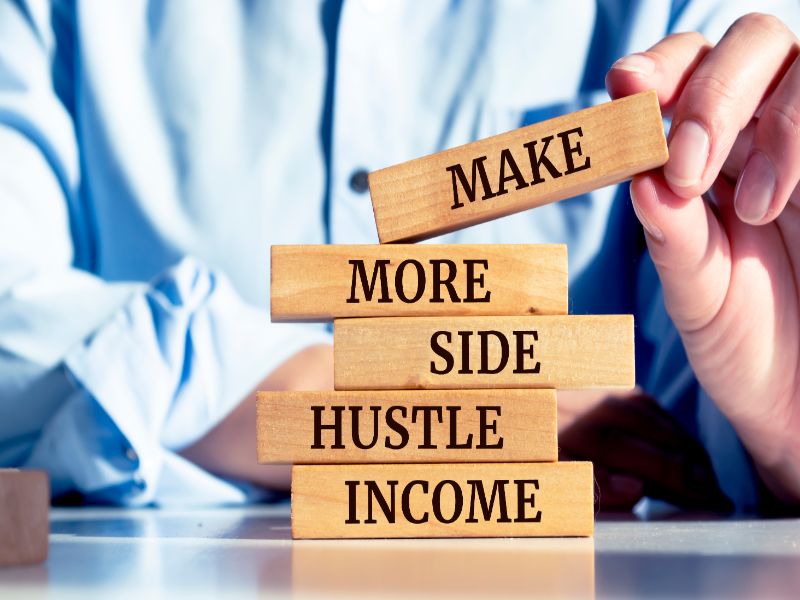 Man holding a wooden block with "Make more side hustle income" message