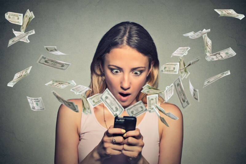 Shocked woman using smartphone dollar bills flying away from screen