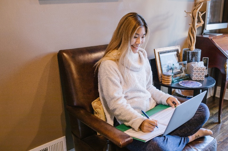 Woman Writing While Smiling in Front of the Laptop