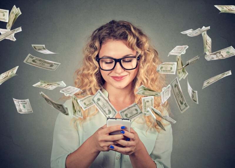 Woman using smartphone with dollar bills flying away from screen