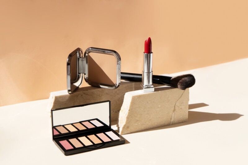 Minimal modern cosmetic scene with make up brushes, eye shadows palette, lipstick, neutral beige background