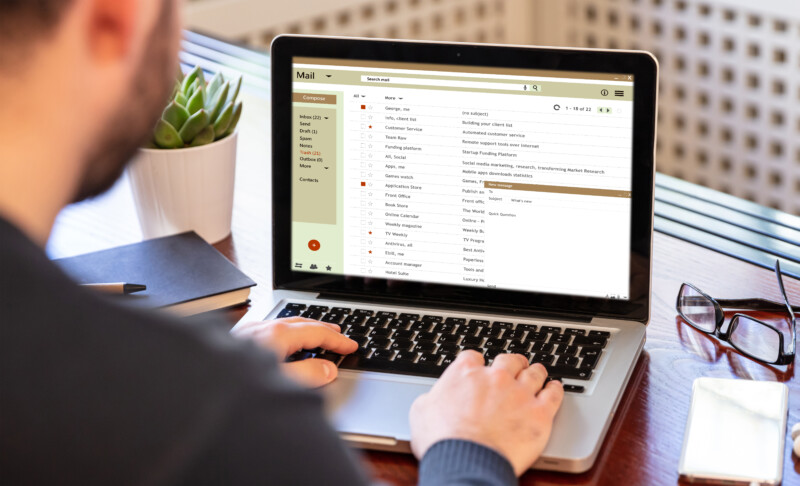 Email inbox message list on a computer laptop screen, man working on an office desk, business background