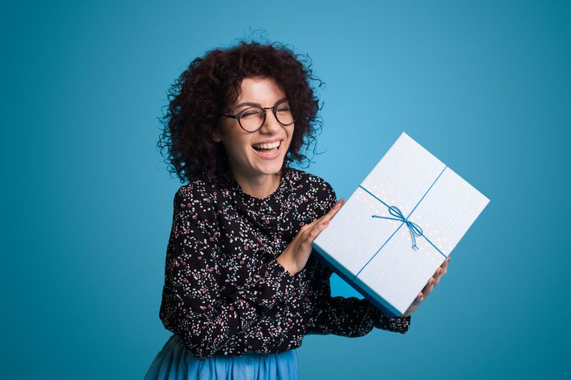 Happy curly haired girl wearing eyeglasses receiving gift box