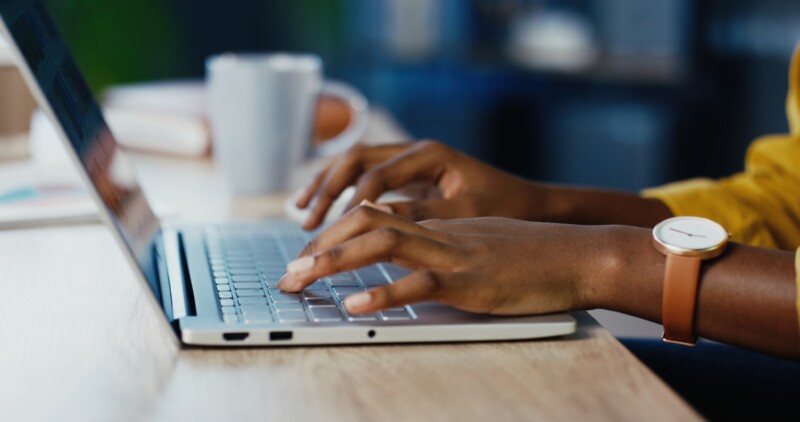 Close up shot of African American female hands typing on laptop while sitting