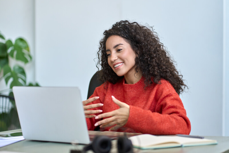 Happy young latin business woman employee, hr manager having remote videocall work hybrid meeting or job interview talking to team or partner looking at laptop on virtual video digital call in office