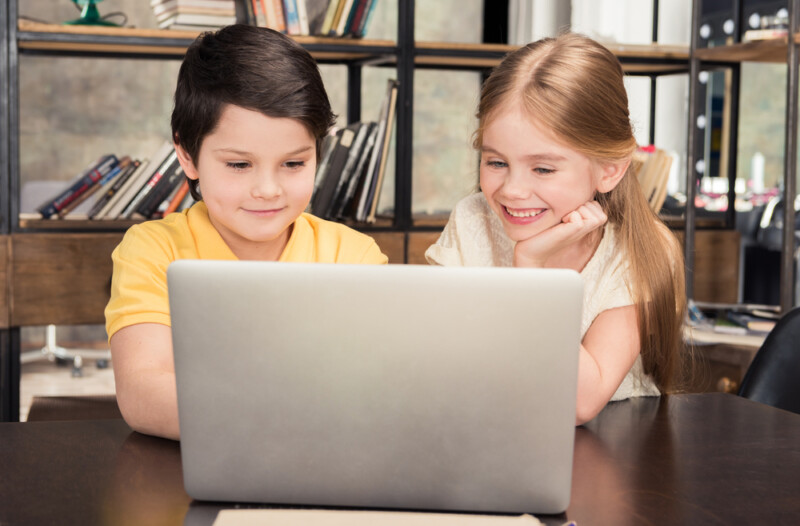 Cute smiling boy and girl sitting at table and using laptop