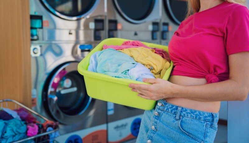 Young beautiful woman washes and dries clothes in the laundry