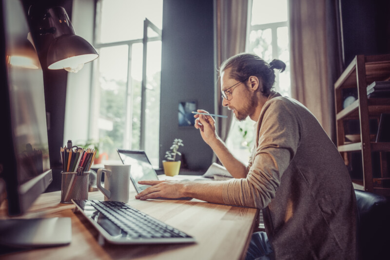 Young freelancer working with laptop at home. Side view of male working on freelance at home office.