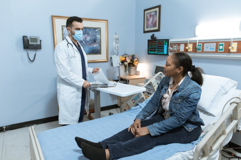 Woman in Blue Denim Jacket Sitting on Hospital Bed