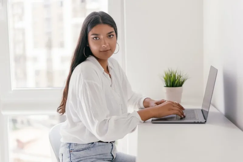 A Woman in White Long Sleeves Sitting while Typing on Her Laptop